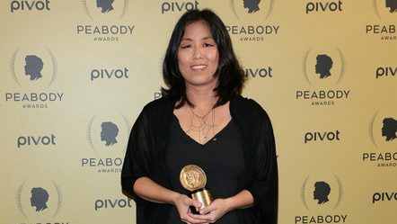 A woman holds her Peabody Award in front of a red carpet backdrop.