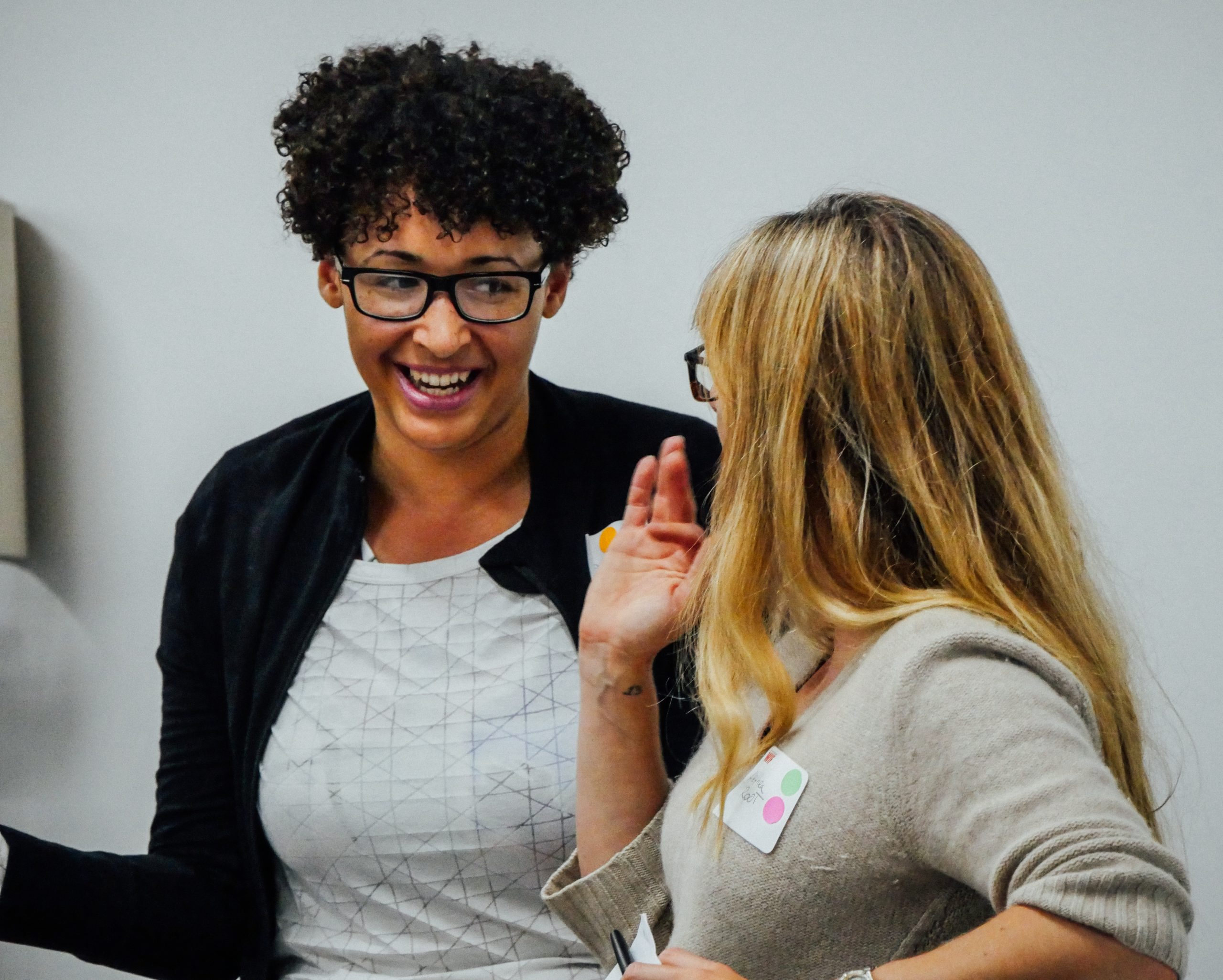 Two women smile as they speak to each other at a party.